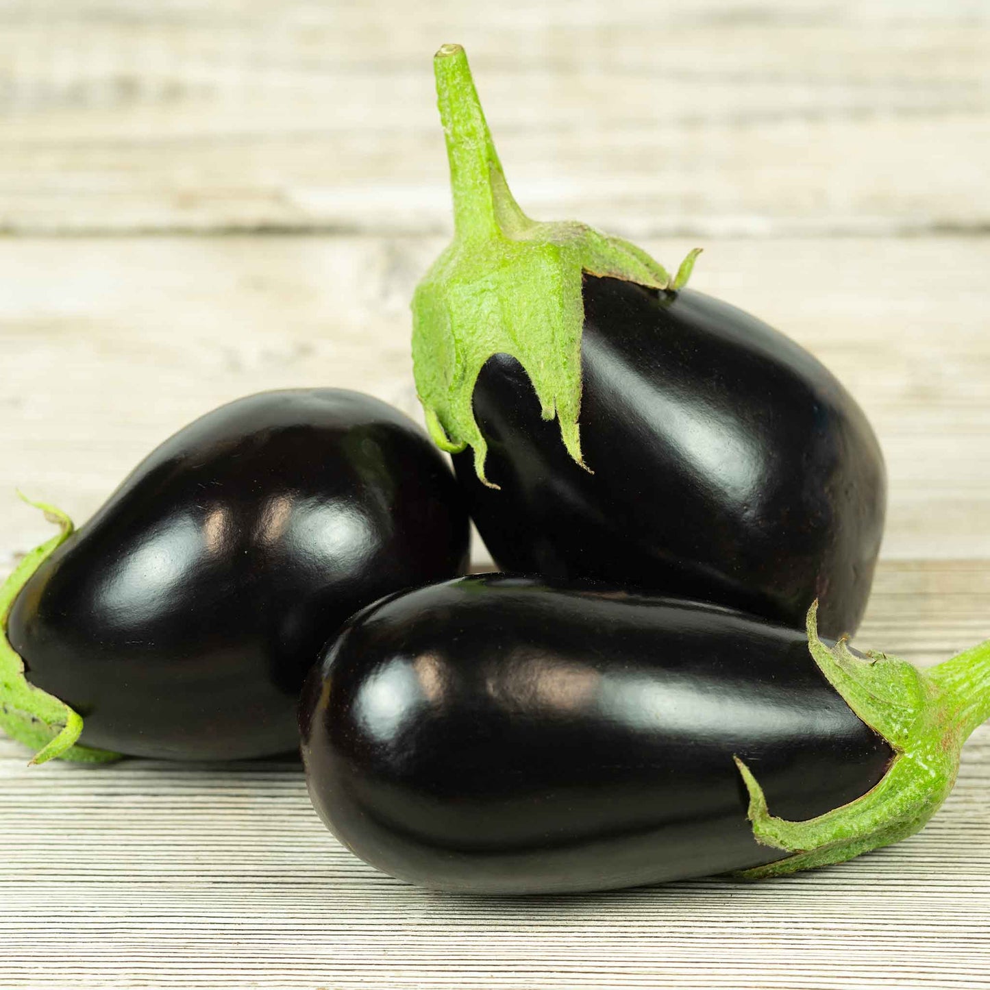 A single, glossy, Black Egg eggplant with a green stem, against a wooden background.