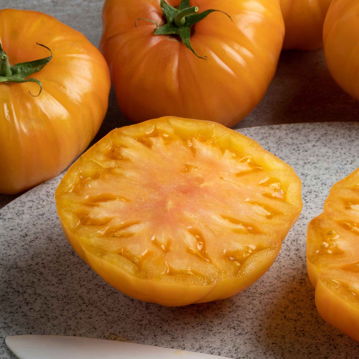 A ripe, orange persimmon tomato sliced, with whole tomatoes in the background.