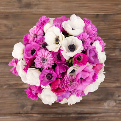 A cluster of pink and white Adeline anmeone flowers agianst a wooden table.