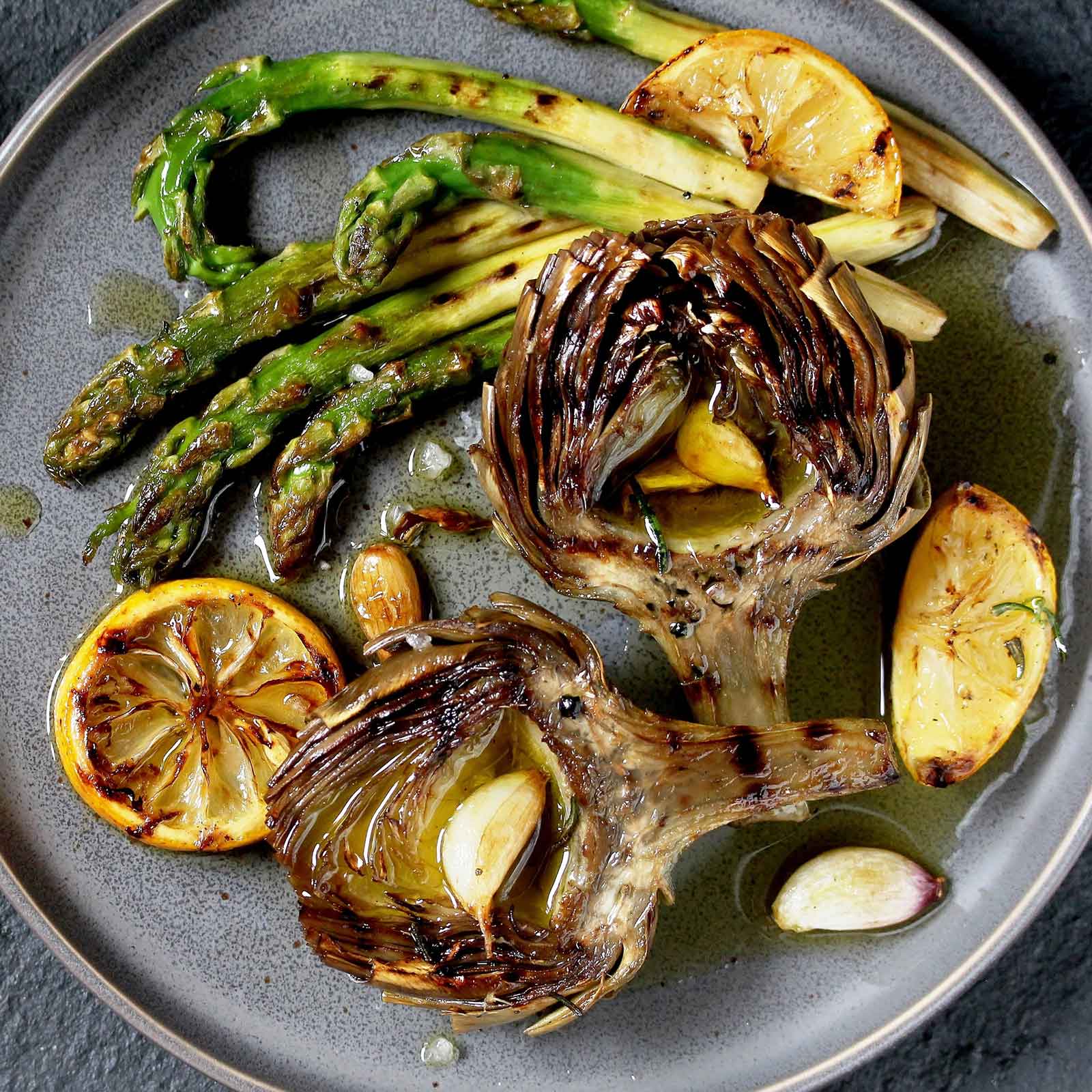A plate of grilled green globe artichoke with other grilled and cooked vegetables.