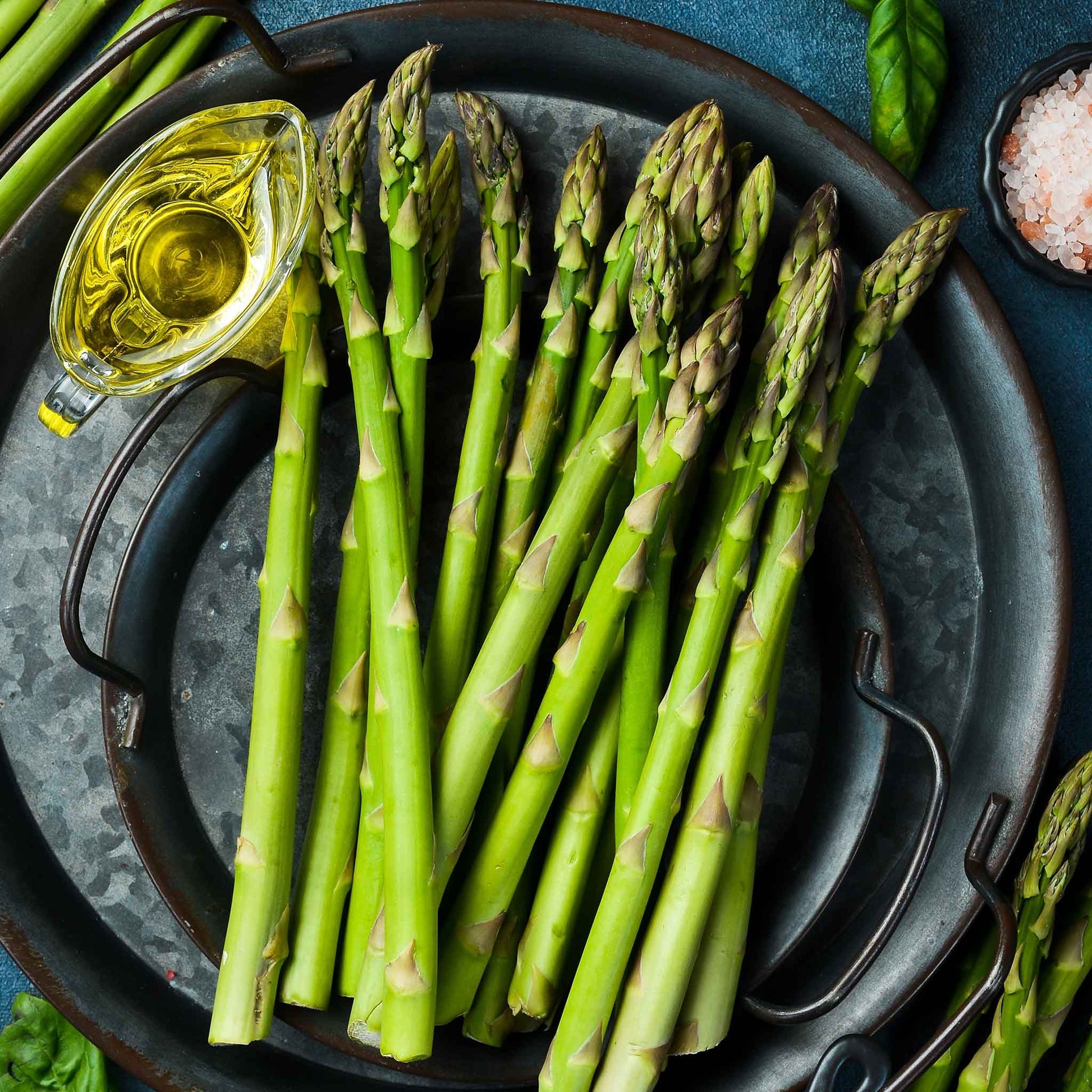 A plate of cooked mary washington asparagus with a bowl of oil for dipping.