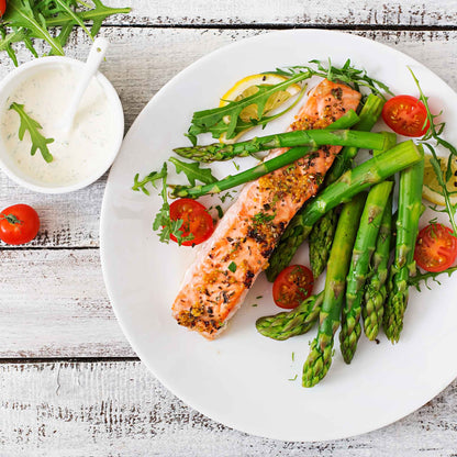 A plate of cooked salmon and mary washington asparagus and tomatoes ready to eat.