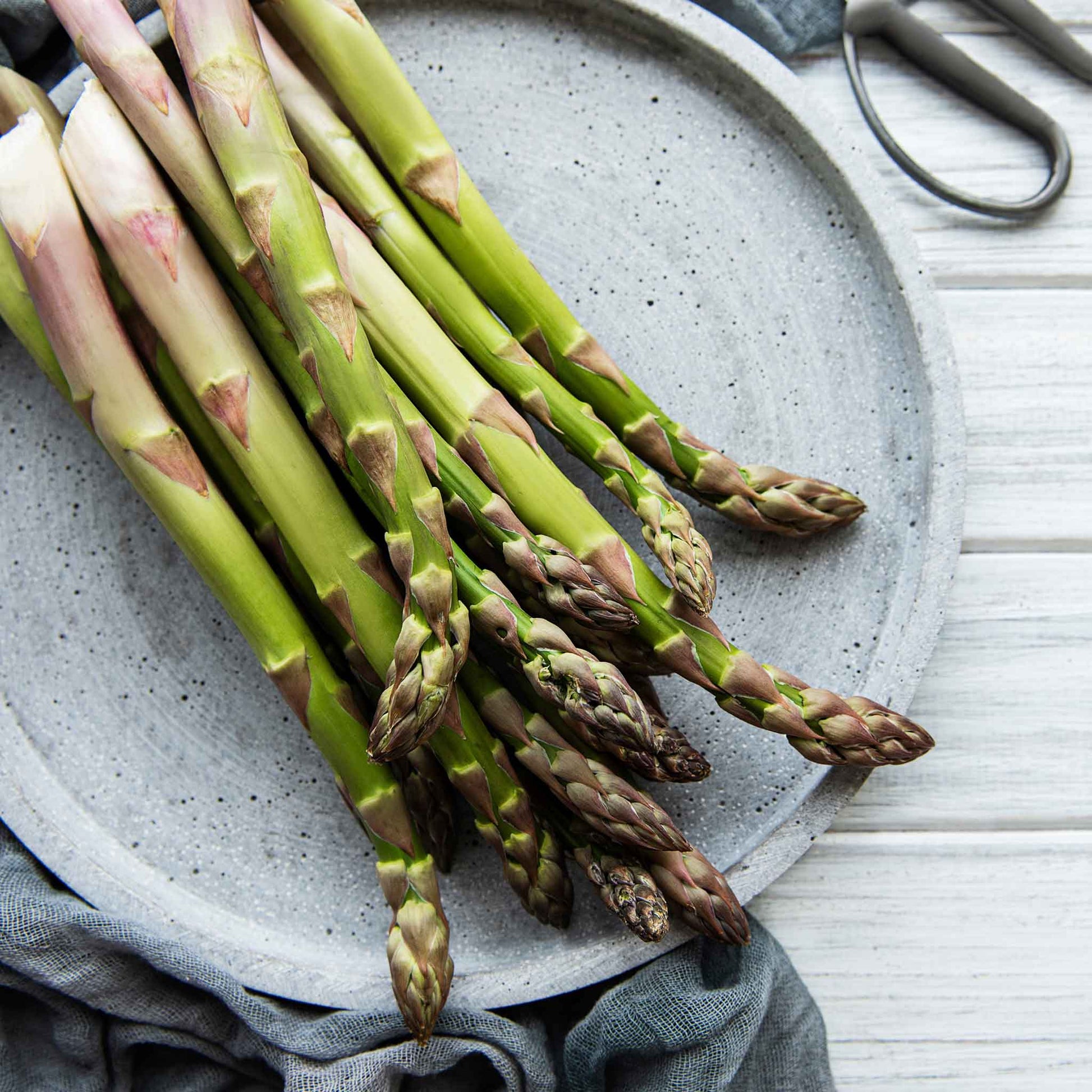 A close-up shot of several bright green asparagus spears with purple tips on a plate.