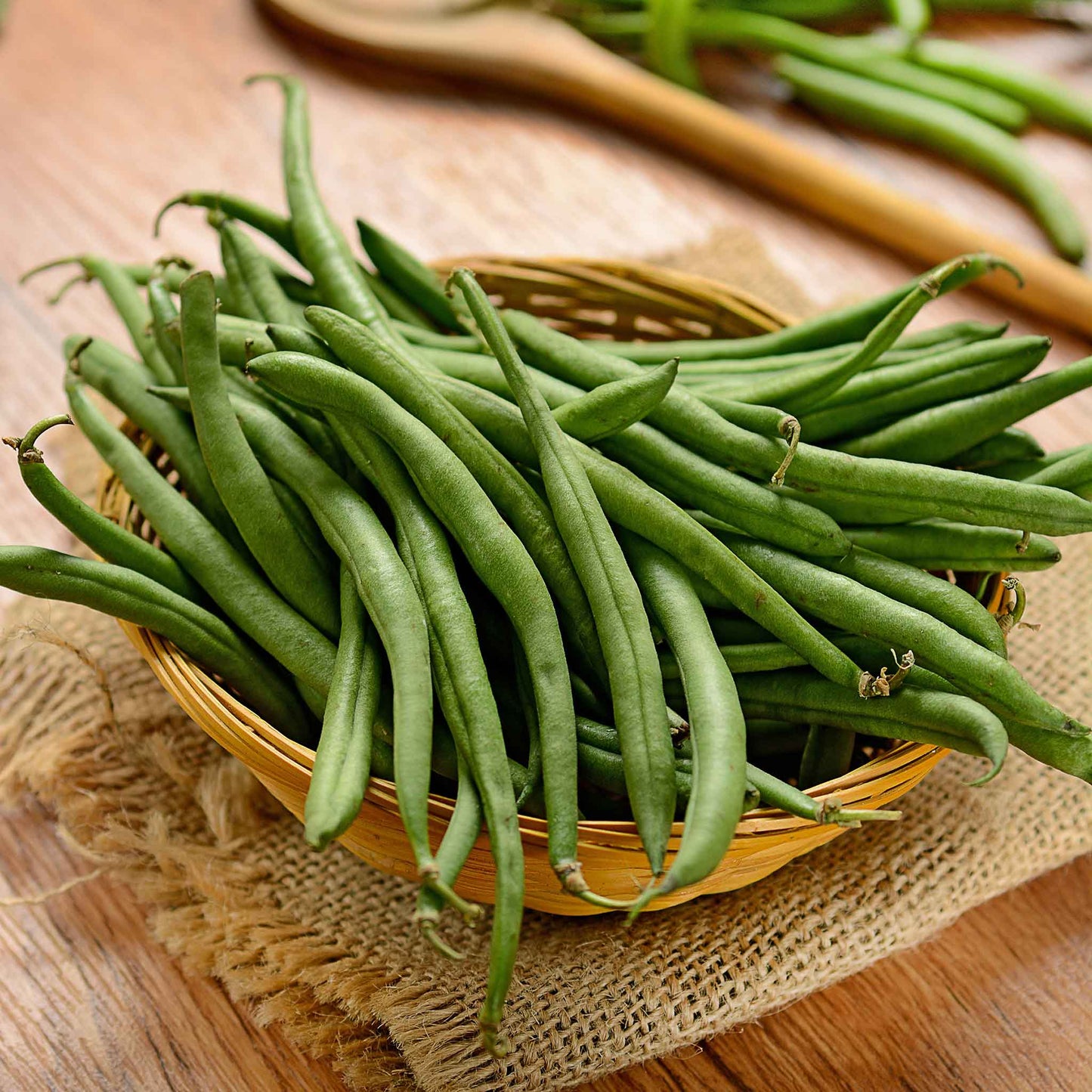 A close-up shot of several burpee stringless beans in a wooden bowl on a wooden surface.