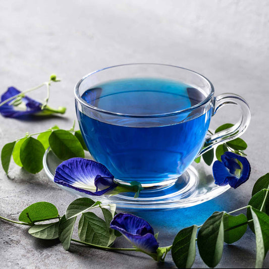 A close-up shot of a vibrant blue butterfly pea flowers with leaves and a cup in the background