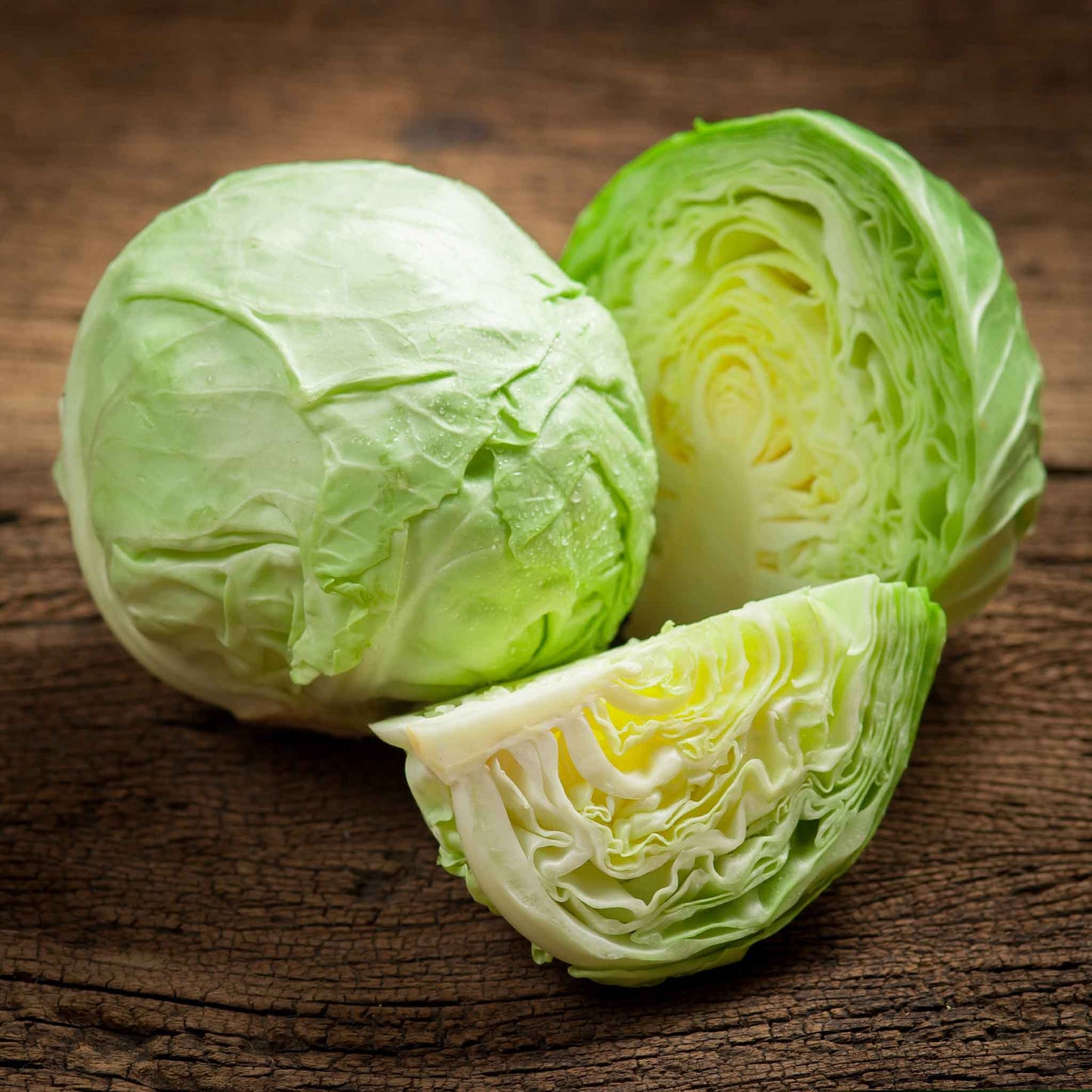 A large, round, vibrant green cabbage head of the All Seasons variety on a wooden surface.