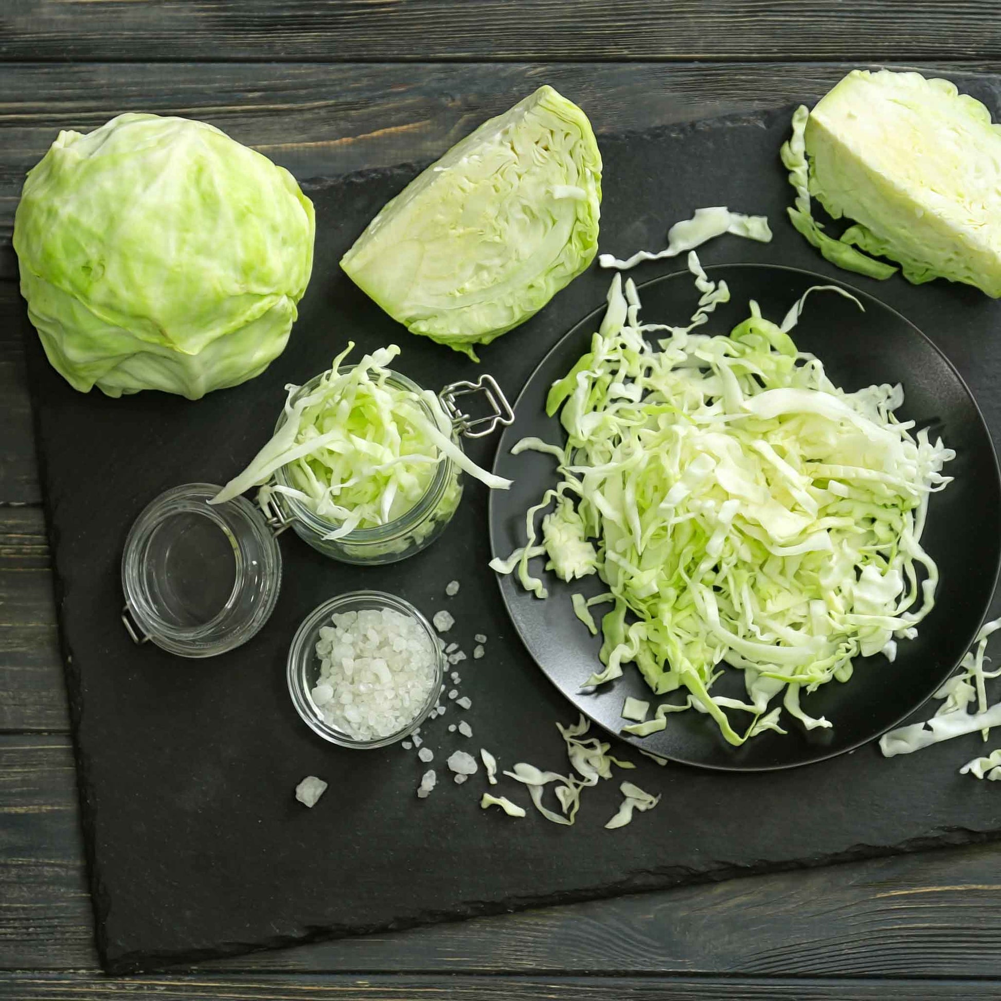 Golden Acre cabbage whole, halved, and shredded on a black background.