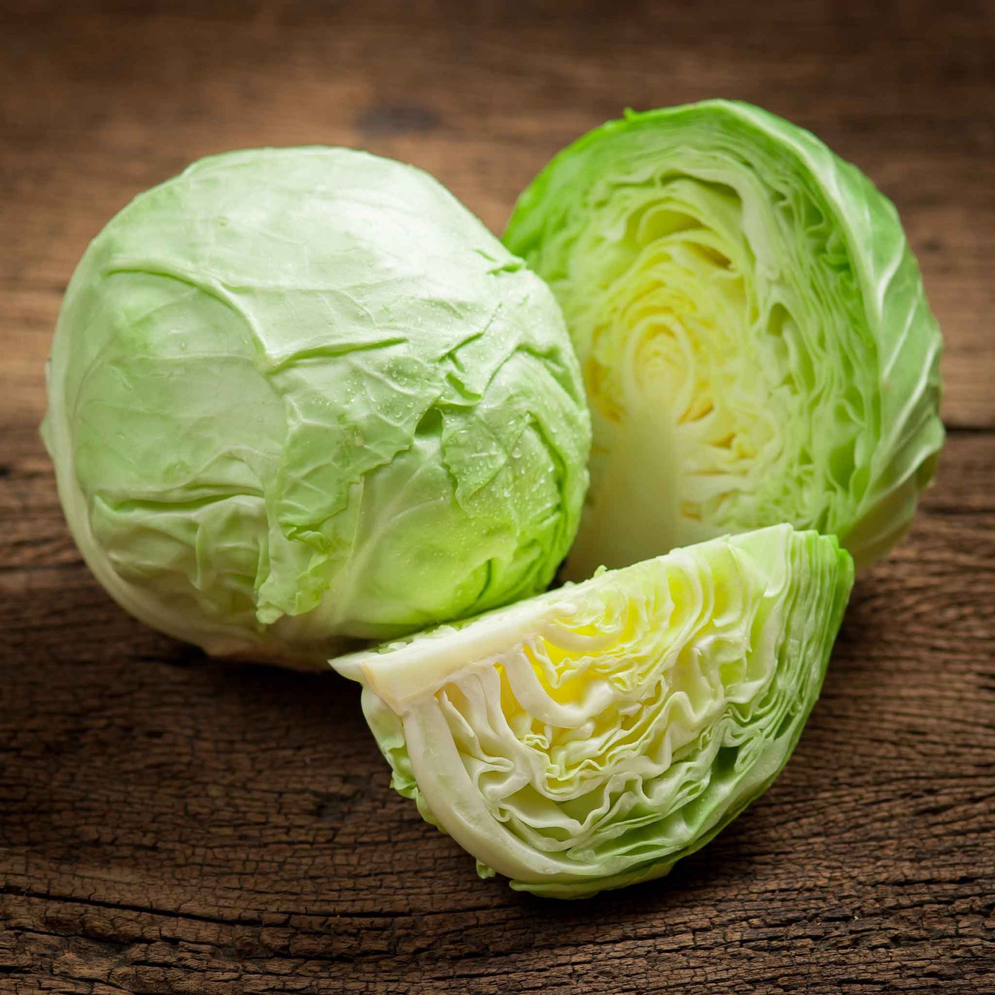 Golden Acre cabbage whole and halved on a dark background.