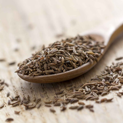 Caraway seeds, a common ingredient in baking and cooking, are scattered on a neutral surface.