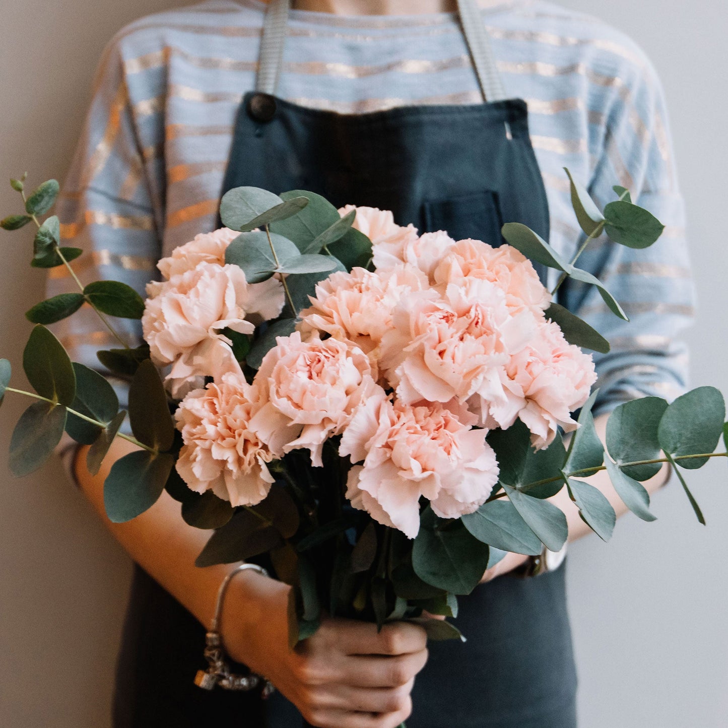 Pink La France Carnations in a bouquet held by a person in a grey apron outdoors.