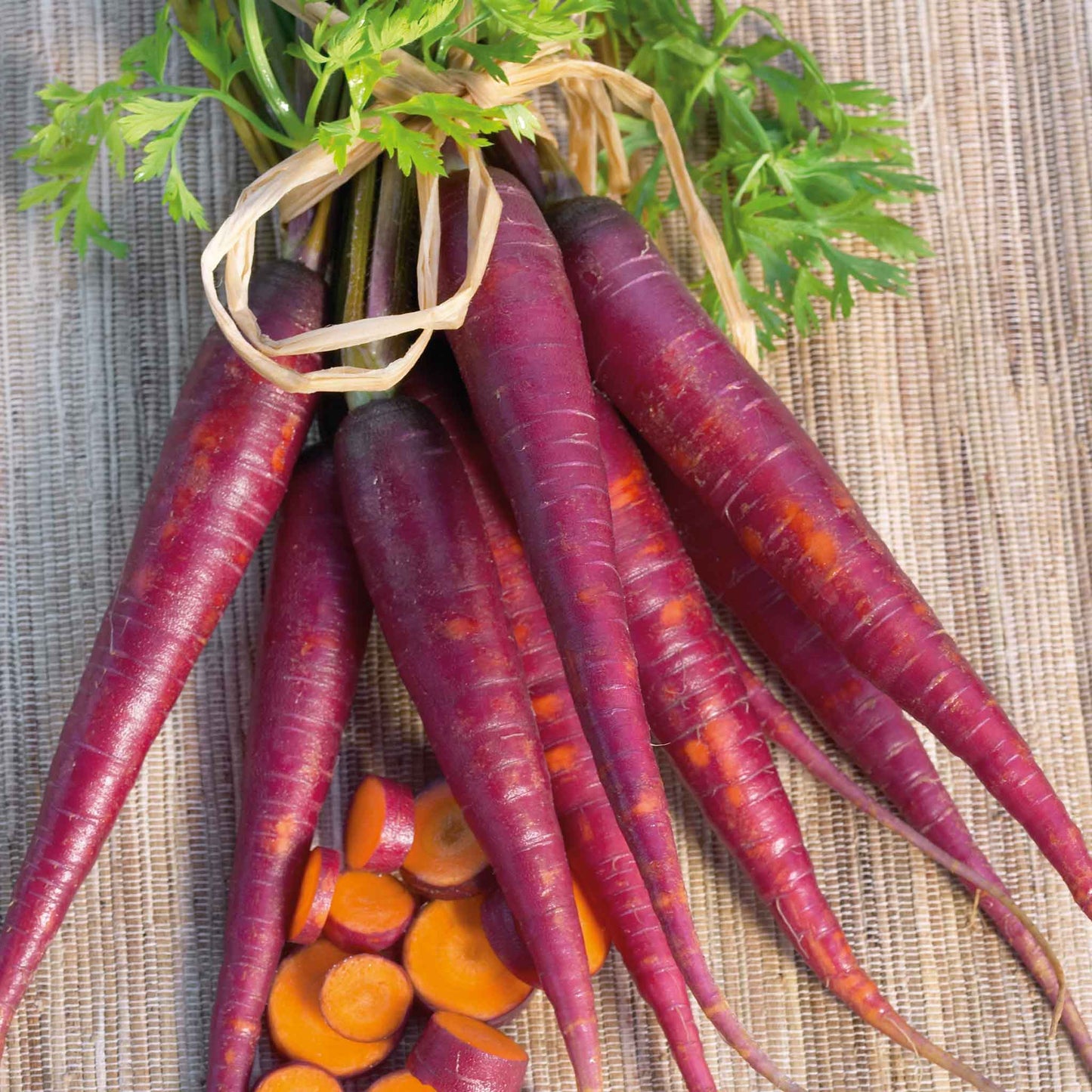 A bunch of cosmic purple carrots with green tops are lying on a wooden surface, ready for harvest.