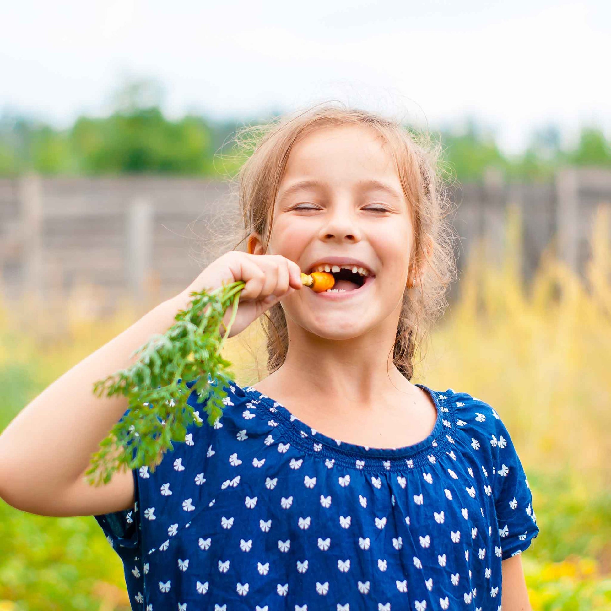 A child eating a Little Finger carrot in a garden setting.