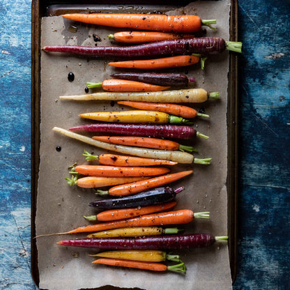 A rainbow blend of orange, yellow, and purple carrots are displayed close-up, highlighting the variety.