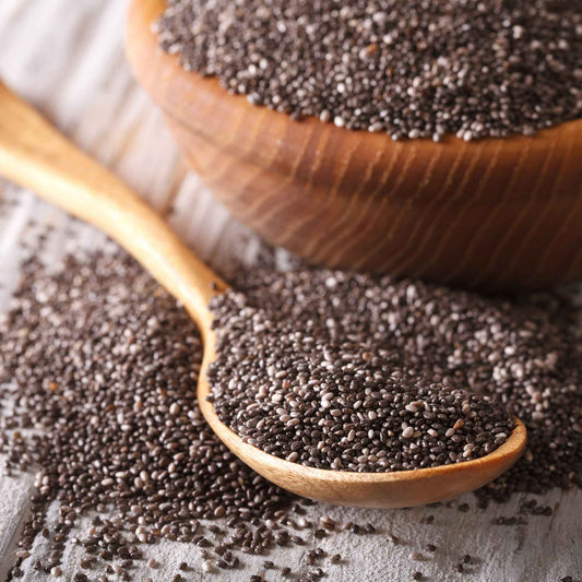 A close-up of a wooden cup filled with tiny black and white chia seeds, showcasing their texture.