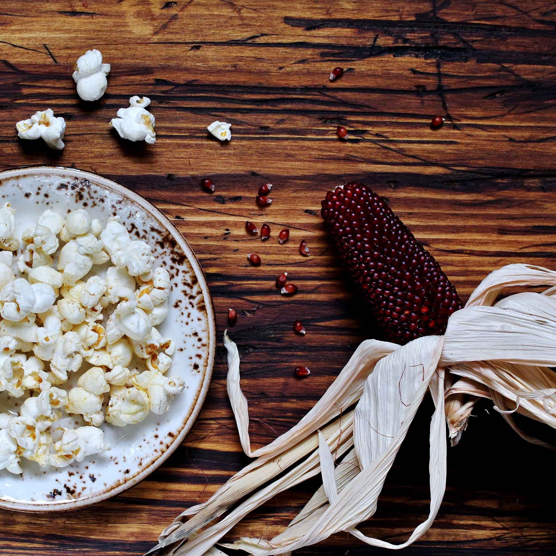 A close-up of a small, red, ripe strawberry popcorn cob on a wooden background.