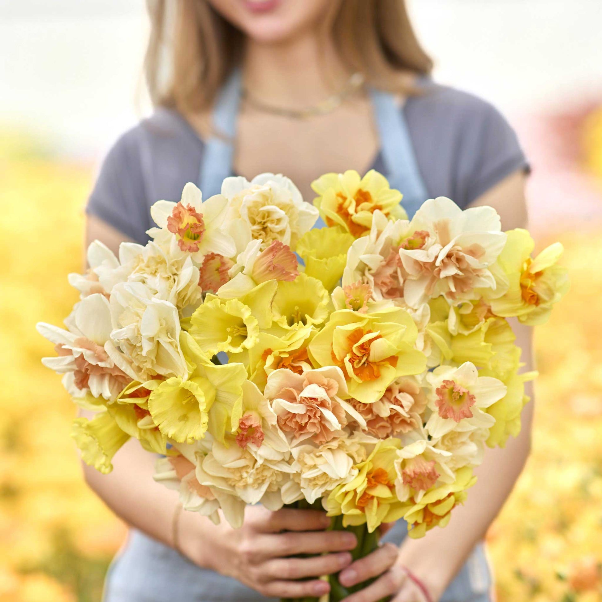 Person holding a bouquet of yellow and white citrus sorbet daffodil flowers with a blurred background