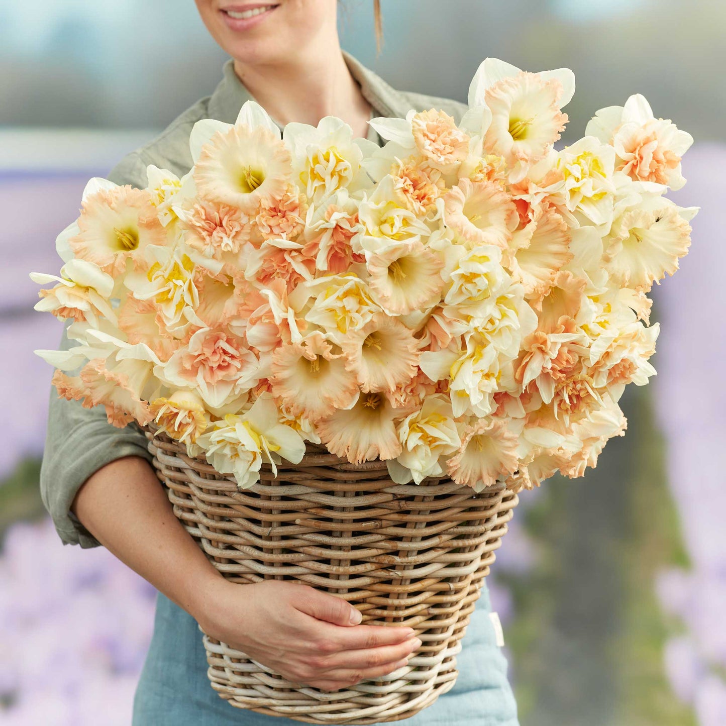 A person holding a basket bouquet of Evelyn's Mix daffodil flowers in a garden setting.