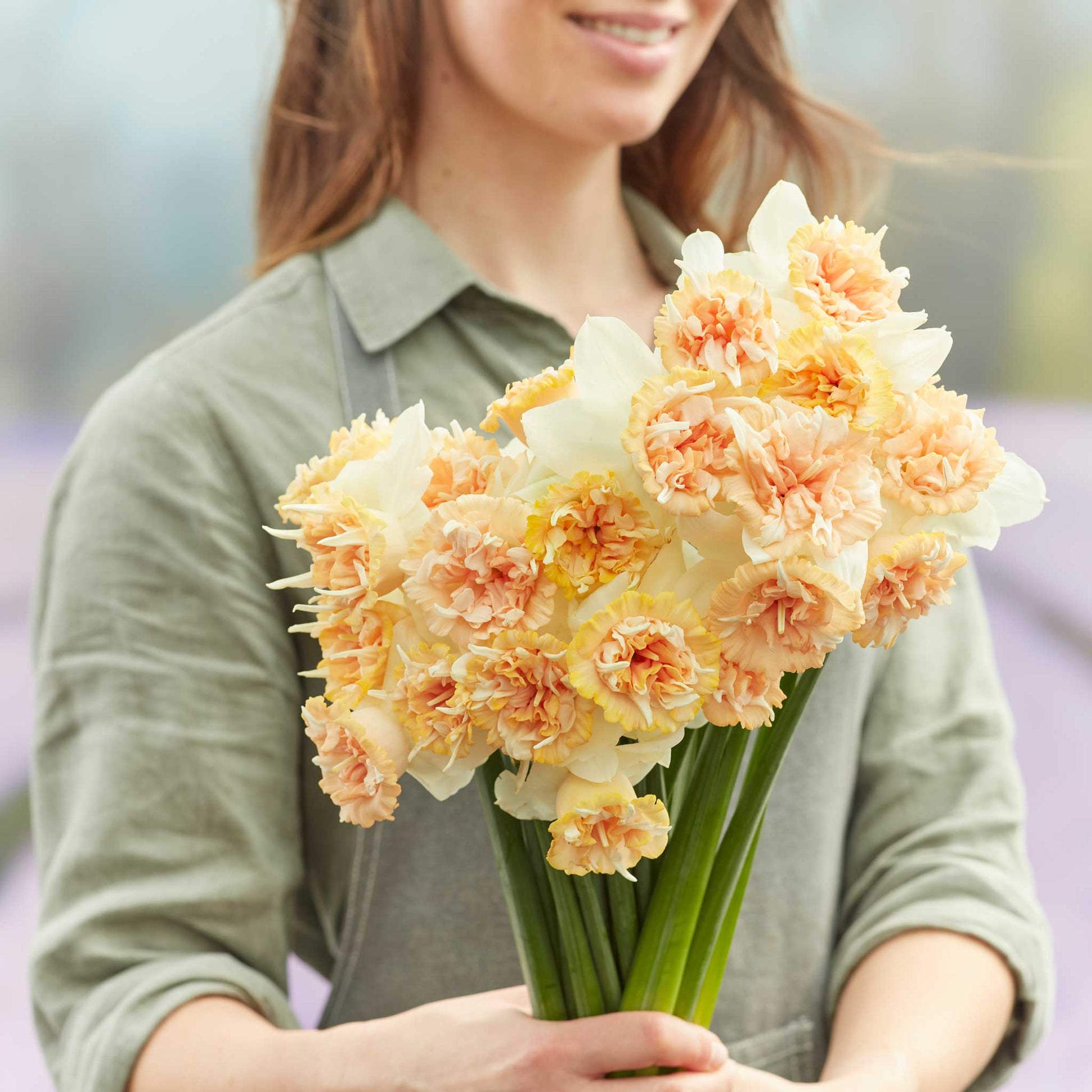 A person holding a bouquet of Petit Four daffodil flowers in a garden setting.