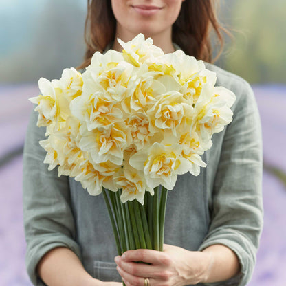 A person holding a bouquet of White Lion daffodil flowers in a garden setting.