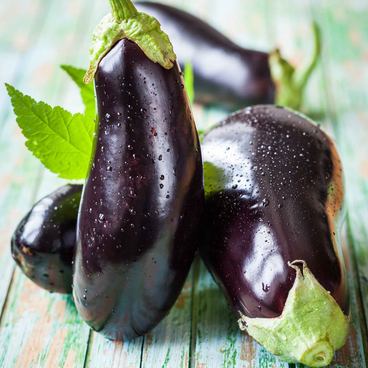 A dark purple, glossy eggplant with a green stem is shown against a wooden background.