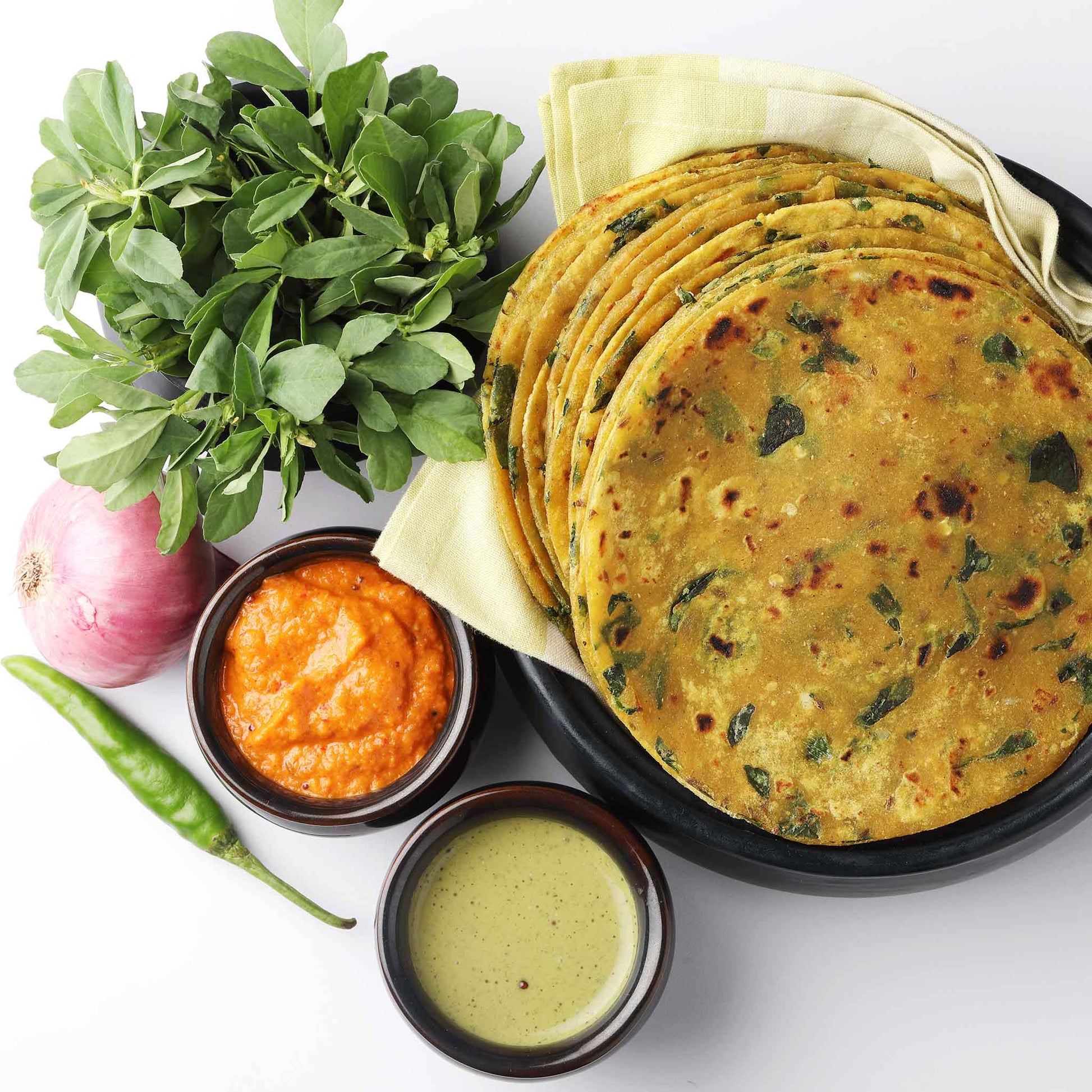 A close-up shot of fresh fenugreek leaves next to several dishes using fenugreek as an ingredient.