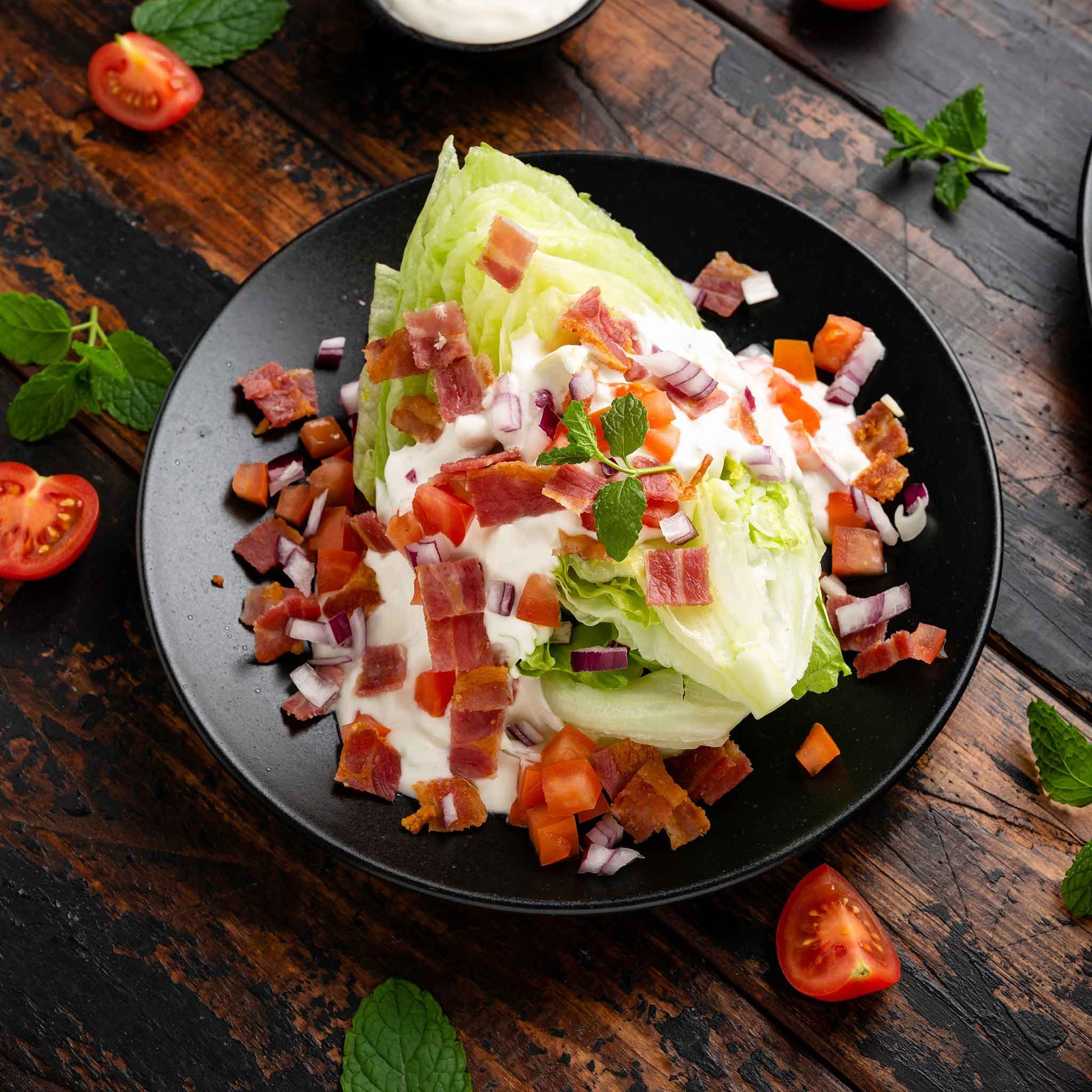 Iceberg lettuce used in a wedge salad topped with tomatoes and dressing on a dark plate.