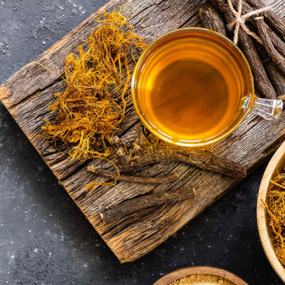 Sprigs of dried licorice root next to licorice tea and dried yellow flowers.