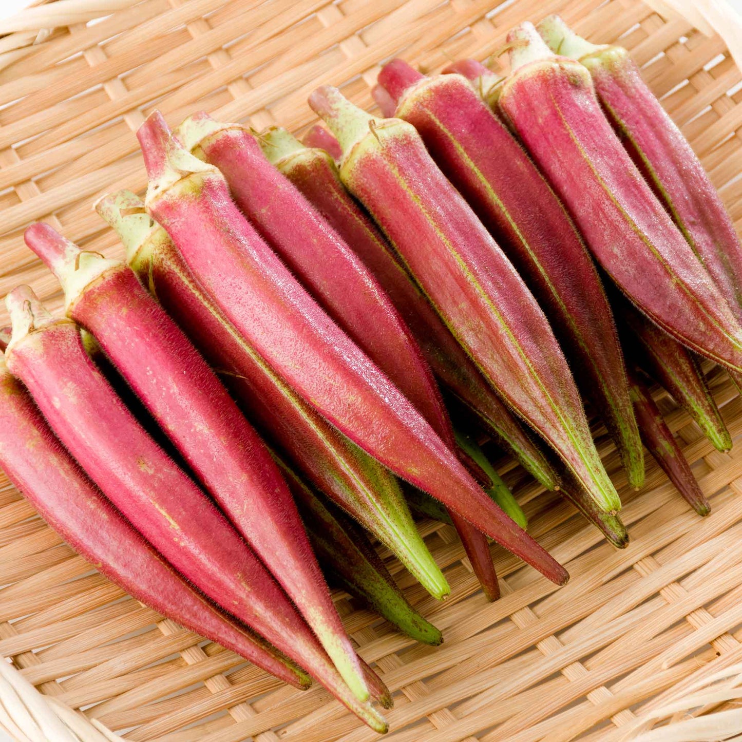 Vibrant Jing Orange okra pods with red skin and green ends on a wicker background.