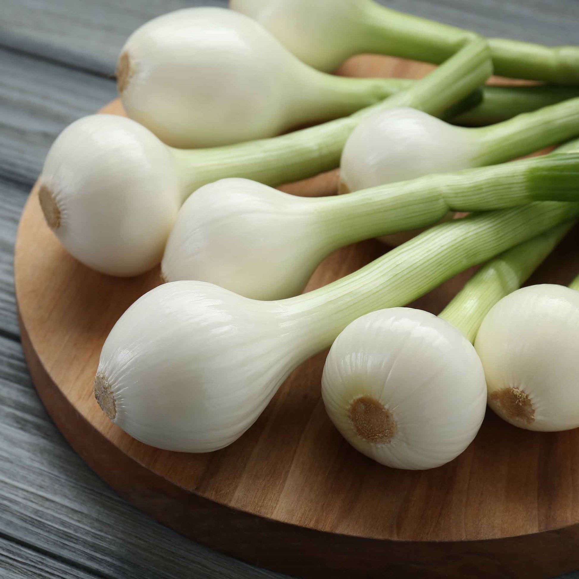 A close-up shot of small, white, Crystal White Wax onions with thin skins on a wooden board.
