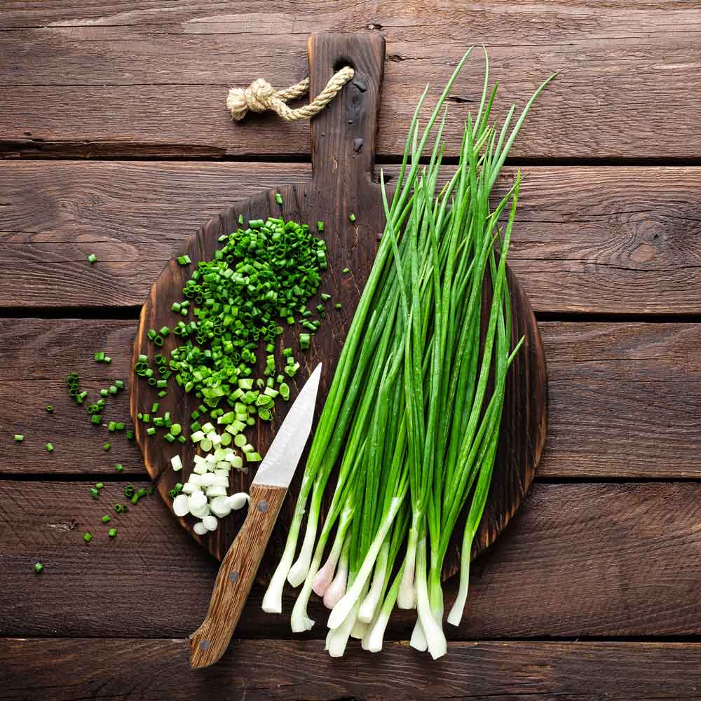 A close-up view of vibrant green Parade Bunching onion shoots with white bases on a wooden surface.