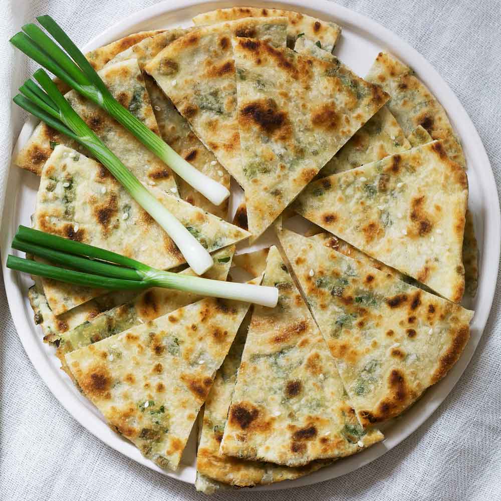 Close-up of green Parade Bunching onion stalks with white bulbs and green shoots on grilled bread.
