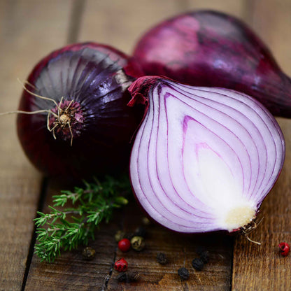 Several vibrant Red Carpet onions with a papery skin and vibrant interior, resting on a white background.