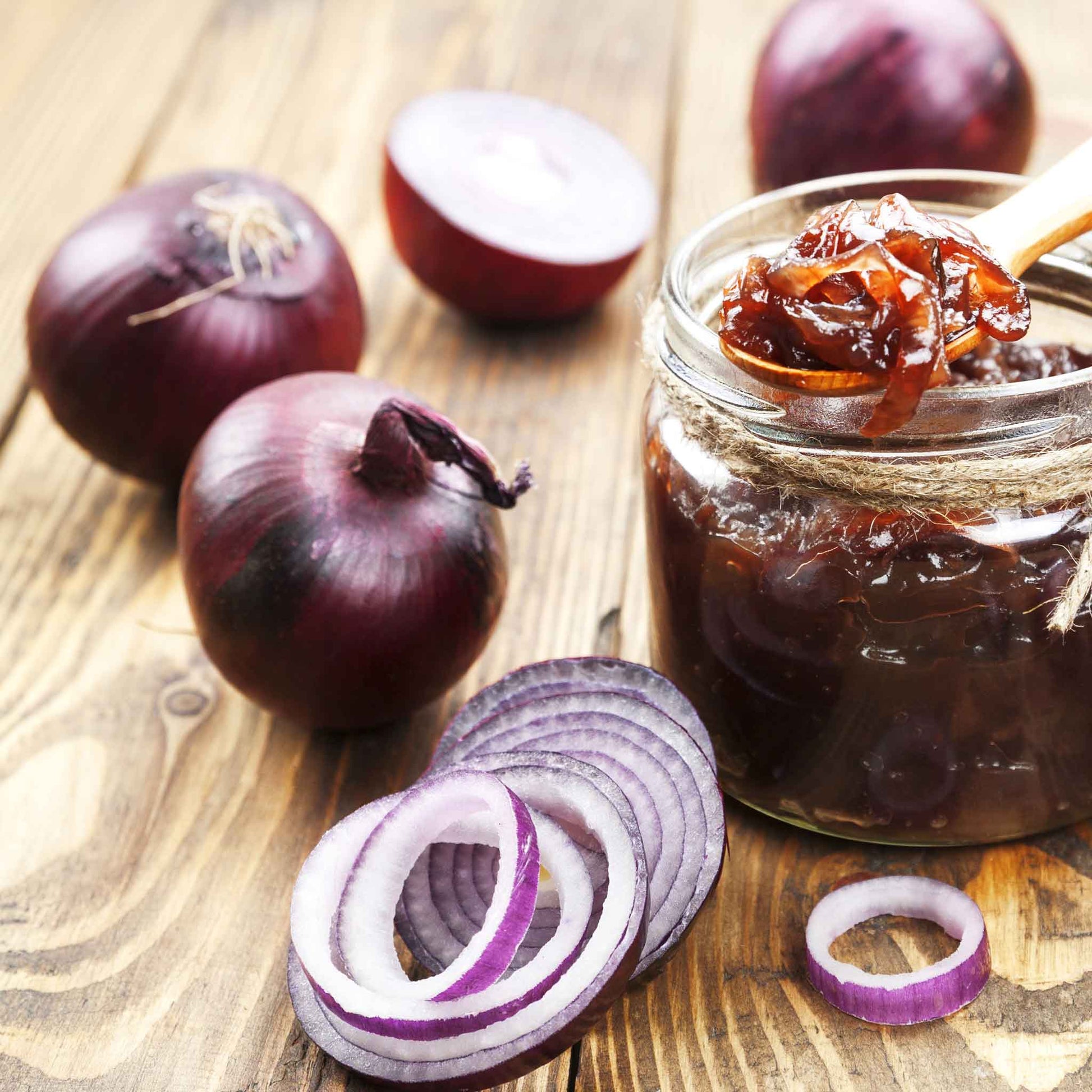 A close-up of several sliced Red Carpet onions with thin, papery skins, resting on a rustic wooden surface.