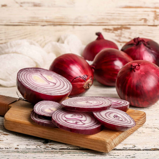 Vibrant Red Creole onions on a wooden background with several sliced onions in the foreground.