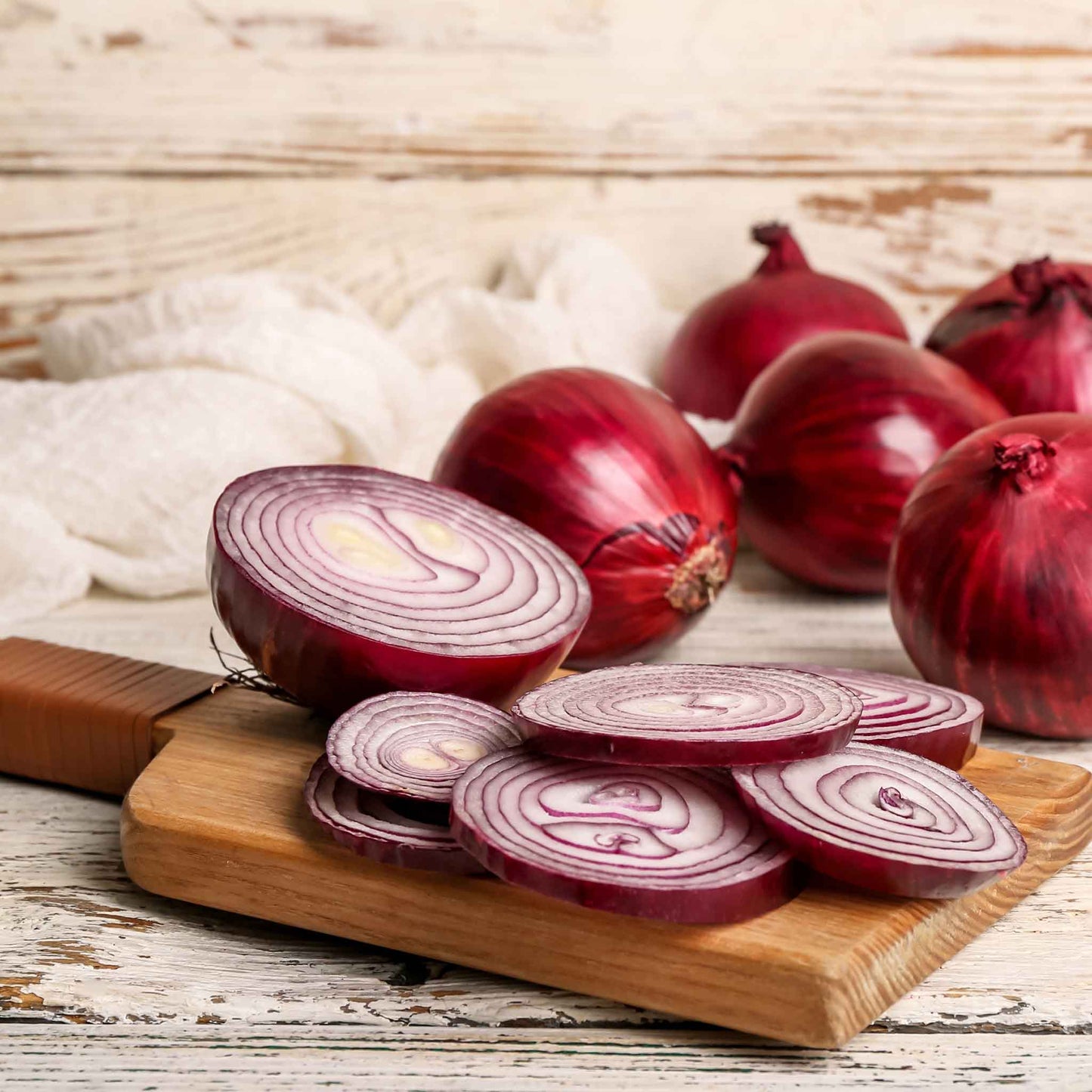 Vibrant Red Grano onions on a wooden background with several sliced onions in the foreground.