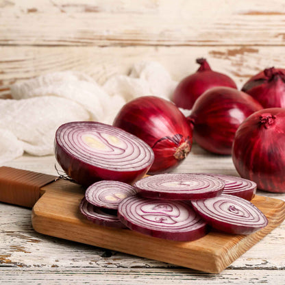 Vibrant Red Grano onions on a wooden background with several sliced onions in the foreground.