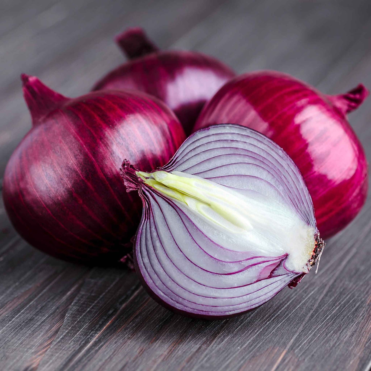 Several vibrant ruby red onions with a papery skin and vibrant interior, resting on a white background.