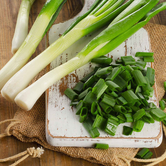 A close-up of a bundle of Tokyo Long White onions with white bases and long green stalks next to some stocks cut up.