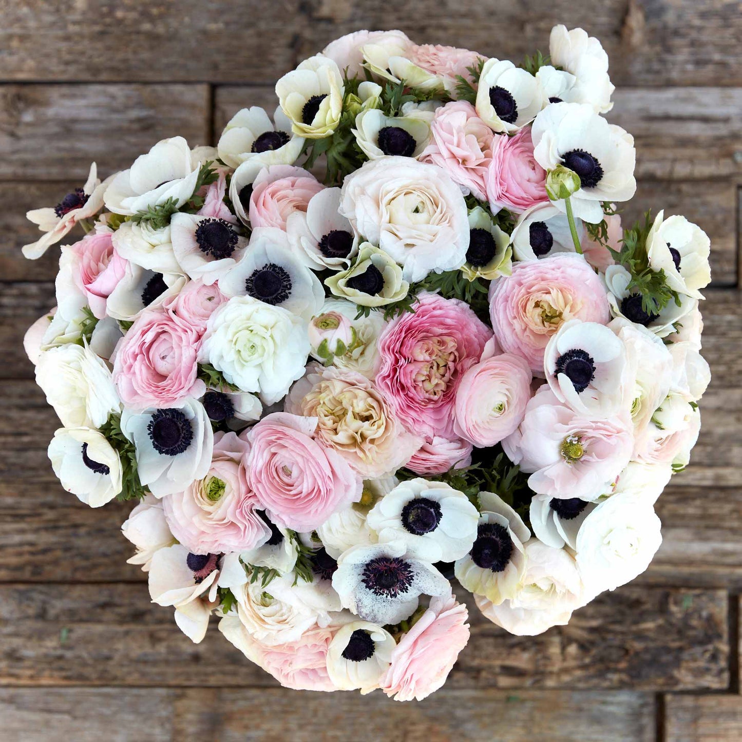 A bouquet of Paris in Spring anemone and ranunculus flowers with a mix of pink, white, and beige petals.