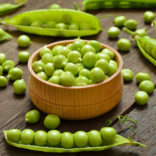 A bowl of shucked Thomas Laxton peas on a wooden surface.