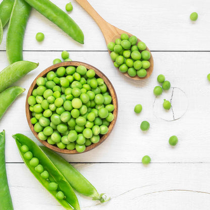 A bowl and spoon full of Wando peas on a white surface.