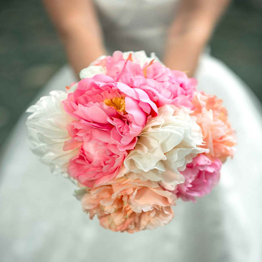 A person holding a bouquet of jumbo bridal bouquet peony flowers with a blurred background.