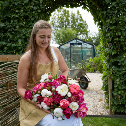 A person holding a bouquet of pink and white mix peony flowers with a natural background.