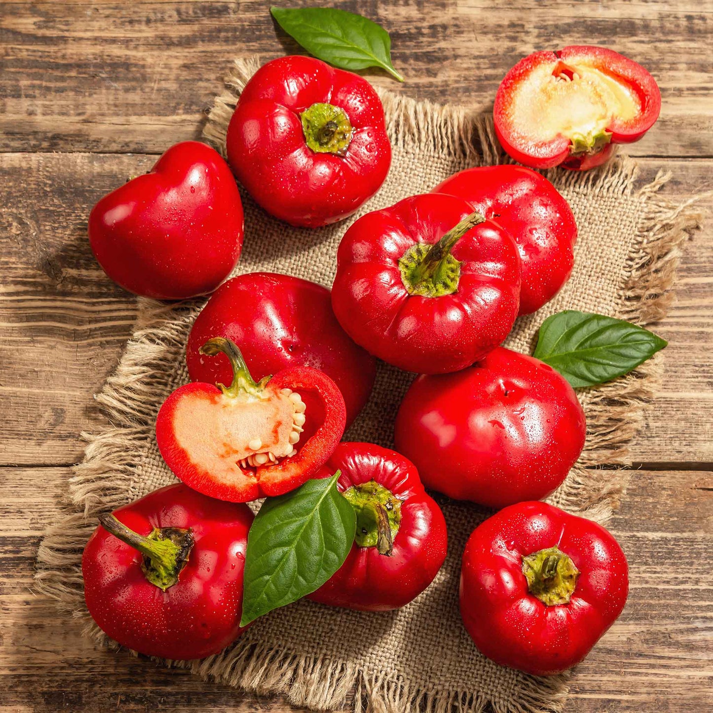 A group of whole and halved Alma Paprika peppers with glossy red skin and green stems.