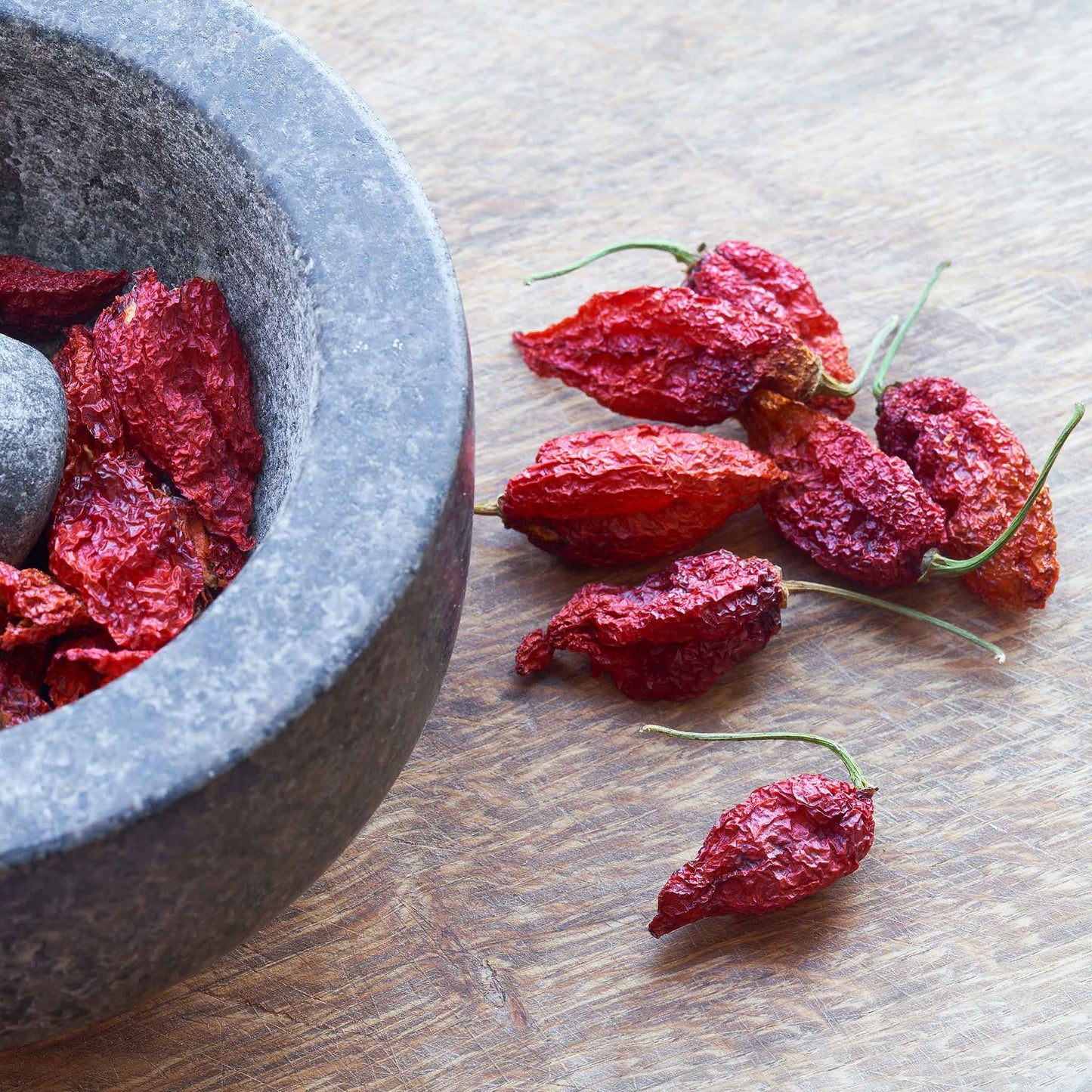 Several shriveled, bumpy, red Bhut Jolokia 'Ghost' peppers laid out next to a bowl ready for use.