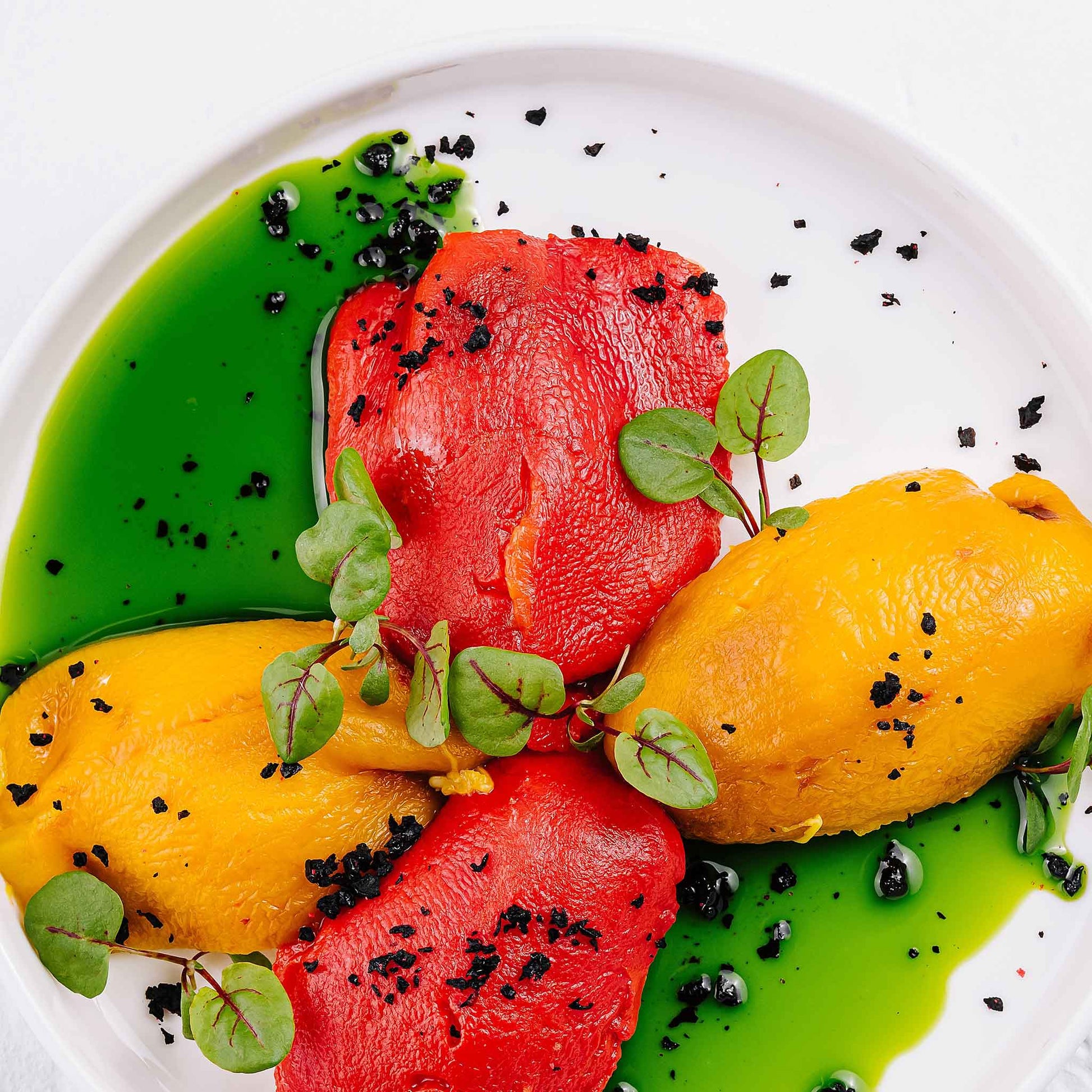 Roasted Canary Bell peppers with other peppers on a plate with a green sauce.