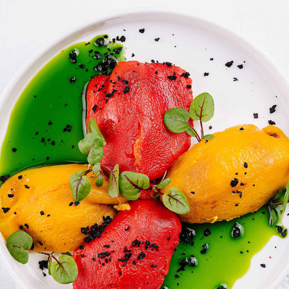 Roasted Canary Bell peppers with other peppers on a plate with a green sauce.