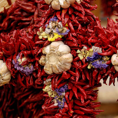 A scattering of Chile de Arbol peppers showing their deep red coloring with a clove of garlic in the center.