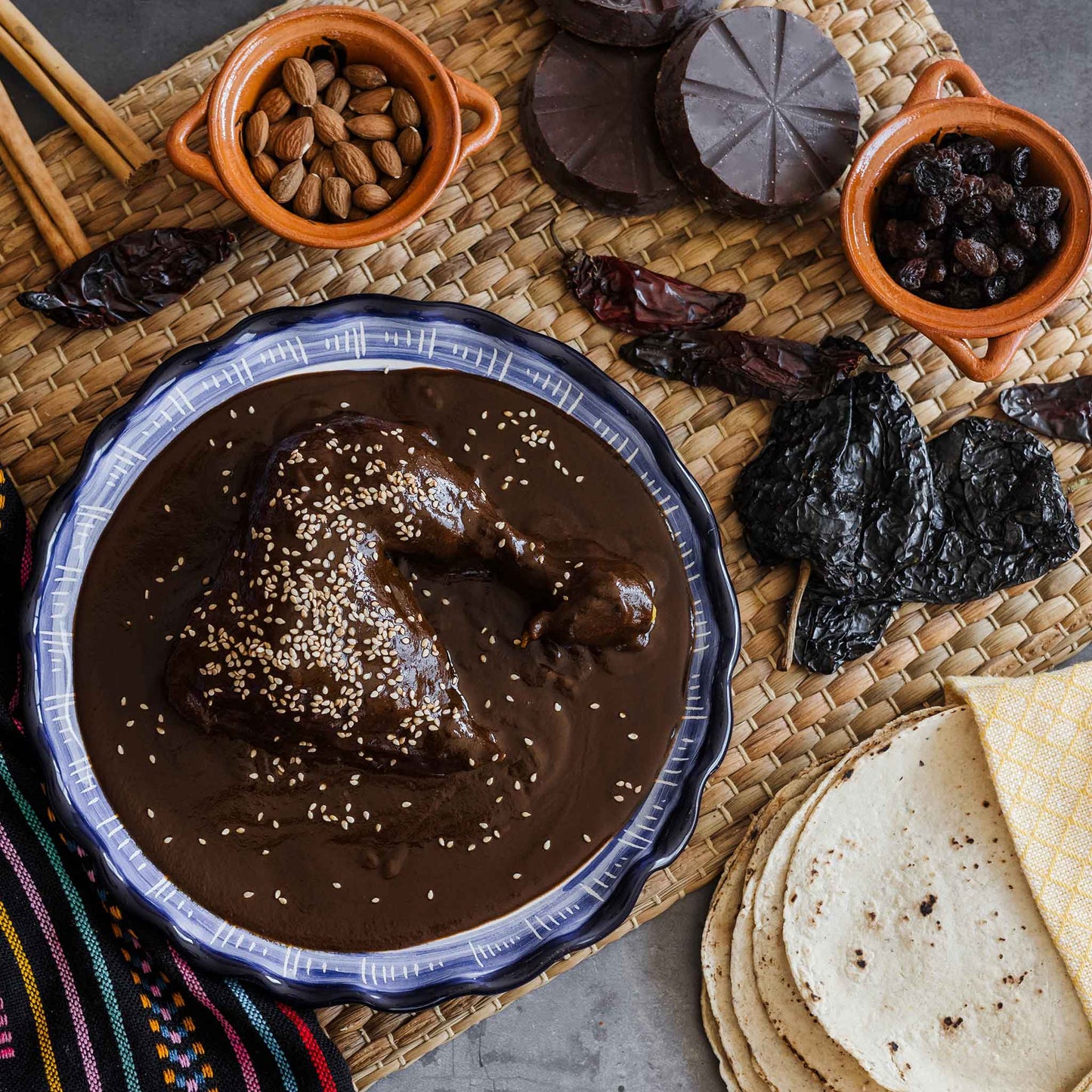 Three dark, almost black, dried Mulato Isleno peppers are shown, with a bowl of processed peppers.