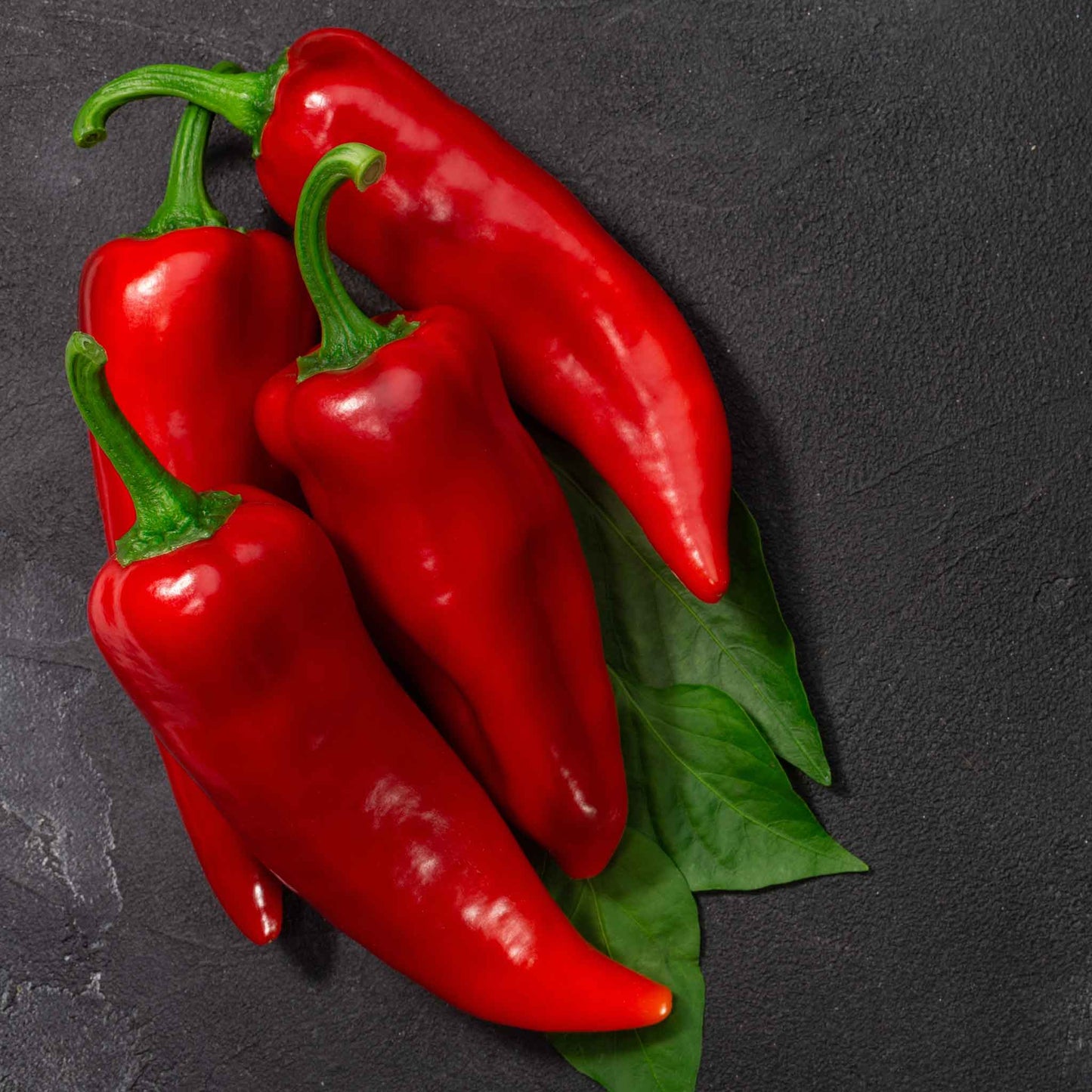 Vibrant red Marconi peppers, elongated and glossy, sits on a dark background.